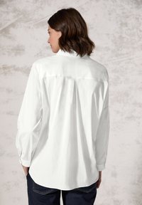 Witte lange mouwen shirt met een ontspannen pasvorm, rugplooidetail en knoopmanchetten, gedragen met donkere denim jeans.