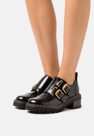 Black patent leather shoes with three gold buckles, chunky rubber outsole, and a raised block heel. Smooth texture, rounded toe design.