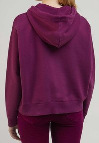 Lila hoodie med huva, sänkta axlar och kort design. Tillverkad av sweatshirtmaterial med en mjuk textur. Enfärgad baksida.