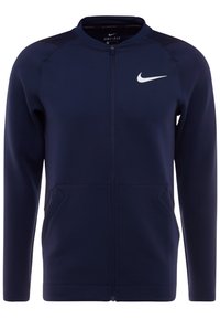 Mørkeblå zip-up jakke lavet af glat, let materiale. Har en høj krave, sidelommer og et hvidt Nike-logo på venstre bryst.