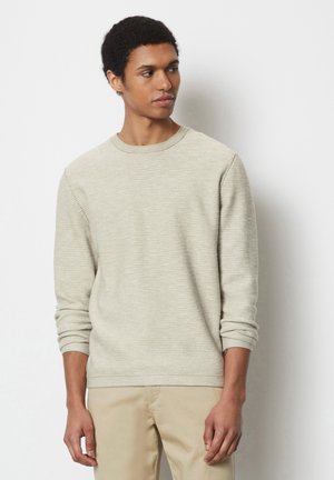 Light beige knit sweater with a crew neckline and long sleeves. Fabric features a subtle striped texture. Paired with beige pants.