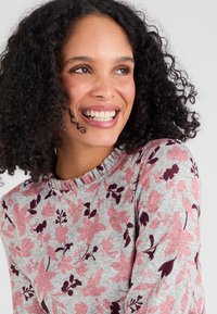 Langarmige, grijze trui met een ribbelhalslijn, met een bloemenpatroon in roze en bordeaux. Zacht, gebreid materiaal.