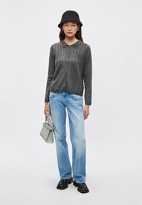 Grijze geribbelde cardigan met knopen aan de voorkant, gecombineerd met lichtblauwe rechte jeans. Zwarte bucket hat en kleine groene handtas maken de look compleet.