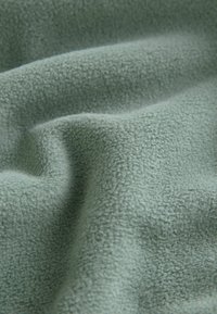 Blødt, tekstureret stof i en dæmpet grøn farve, der har en fuzzy overflade med subtile variationer og viser bløde folder og draperinger.