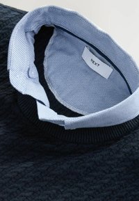 Marineblauer Pullover mit strukturiertem Strickmuster und einem hellblauen gestreiften Kragen. Das Etikett trägt die Aufschrift "NEXT", was die Markenidentität anzeigt.
