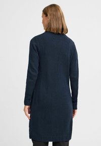 Marinblå lång stickad cardigan med en strukturerad yta, ribbade muddar och fåll. Har en rak silhuett med sidoklyftor för ökad rörelsefrihet.