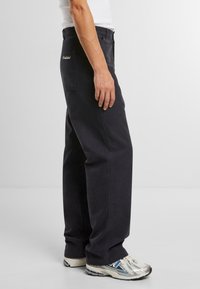 Pantalones de algodón azul oscuro con un diseño de pierna recta, bolsillos laterales y detalle del logo en el bolsillo trasero, combinados con zapatillas ligeras.