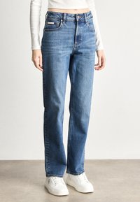 Jeansi din denim albastru cu croială dreaptă, talie înaltă și decolorare subtilă. Au bucle pentru curea și o etichetă cu logo pe spate.