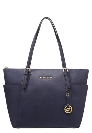 Marineblauwe Michael Kors tote tas met dubbele schouderbanden, twee zijvakken, gouden logo-plaatje en ronde MK-bedel hangend aan één band.