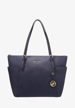 Marineblauwe Michael Kors tote tas met dubbele schouderbanden, twee zijvakken, gouden logo-plaatje en ronde MK-bedel hangend aan één band.