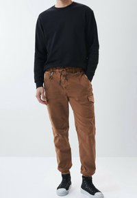 Bruna cargobyxor med elastisk midja, dragsko och sidofickor; kombineras med en svart långärmad sweatshirt och högskurna sneakers.