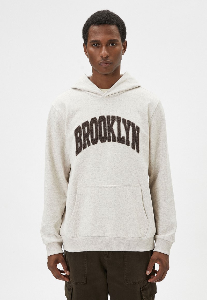 Sudadera gris con un bolsillo frontal, que presenta "BROOKLYN" en texto marrón oscuro. Tejido suave, corte relajado, con capucha ajustable y puños acanalados.