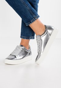 Zilverkleurige metallic sneakers met een gestructureerde afwerking, een ronde neus, een witte rubberen zool en dikke veters. Het ontwerp bevat subtiele naden en accenten.
