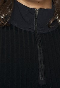 Black ribbed fabric half-zip top with a high collar. Features a smooth zipper closure and textured pattern throughout the material.