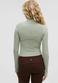 Light green long-sleeve athletic top with a fitted design, high collar, and seam details, paired with brown high-waisted leggings.