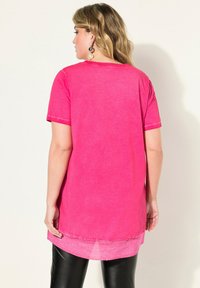 Túnica rosa de manga corta con un dobladillo trasero más largo, fabricada en un tejido ligero, que presenta un sutil degradado en el dobladillo y detalles de costura.
