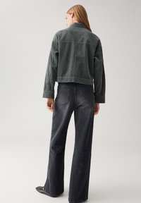 Grijze corduroy cropped jas met een ontspannen pasvorm, gecombineerd met donkere wijde jeans. Heeft een kraag en een subtiele ribbelstructuur.