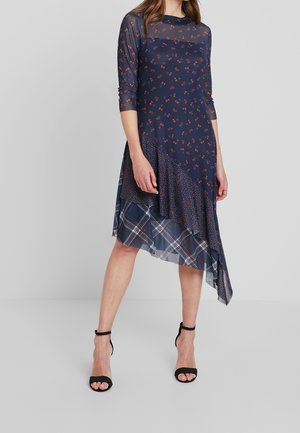 Robe florale marine à manches trois-quarts, partie supérieure transparente, ourlet asymétrique avec motifs écossais et à pois. Tissu léger.