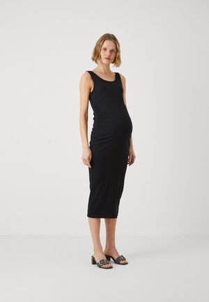 Zwart geribbeld midi-jurkje met een ronde hals en een aansluitende silhouette, met zijdelingse ruches en een eenvoudig, elegant ontwerp. Gecombineerd met zwarte open teen hakken.