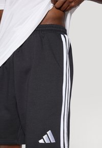 Črne atletske kratke hlače iz nežnega blaga. Na straneh so bele proge in na spodnjem levem delu izvezen logotip. Elastičen pas.