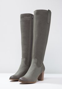 Bottes hautes jusqu'au genou en matériau synthétique gris foncé, avec un design perforé, une fermeture éclair latérale et un talon bloc. Texture lisse et bout arrondi.