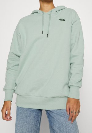 Haut à capuche vert menthe clair en tissu doux, avec une poche avant, un cordon de serrage sur la capuche et un logo noir sur la poitrine.