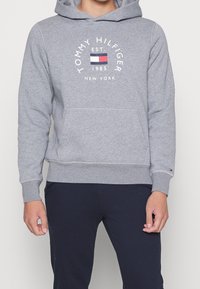 Grauer Hoodie aus Strickstoff, mit einer Fronttasche, gerippten Bündchen und dem "Tommy Hilfiger"-Logo mit mehrfarbigen Akzenten.