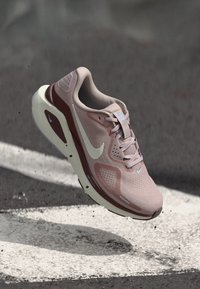 Αθλητικό παπούτσι Nike για τρέξιμο σε ανοιχτό ροζ και μπορντό, με επάνω μέρος από διχτυωτό υλικό, μαλακή σόλα και χαρακτηριστικό λογότυπο swoosh σε λευκό χρώμα.