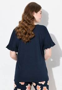 Top blu navy a maniche corte con bordi arricciati, texture liscia e vestibilità rilassata, abbinato a pantaloni fantasiosi con motivi floreali.