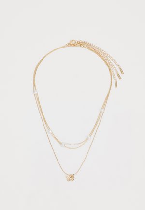 Gold layered necklace with varying chain lengths, featuring white beads and a butterfly pendant at the center. Smooth, shiny texture.