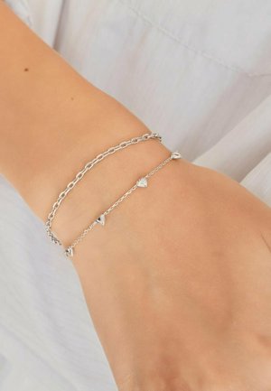 Zwei silberne Armbänder am Handgelenk, eines mit Gliederketten und das andere eine dünne Kette mit kleinen herzförmigen Anhängern.