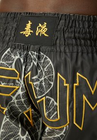 Black athletic shorts with a textured mesh design, featuring a gold embroidered logo and tag with Asian characters along the waistband.
