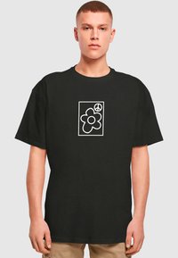 Sorte bomulds t-shirt med et hvidt grafisk motiv af en blomst og et fredssymbol i en rektangulær ramme. Korte ærmer og afslappet pasform.