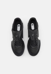 Black sneakers with a leather and suede upper, featuring white Nike swoosh accents, flat laces, and a textured rubber sole.