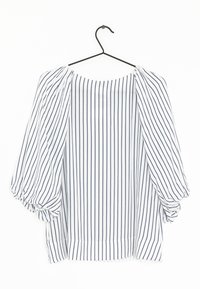 Blouse blanche à rayures verticales bleu marine, avec une coupe décontractée, des manches chauve-souris et un col rond. Suspendue à un crochet noir.