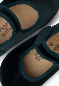 Ballet flats in velluto verde scuro con punta tonda, caratterizzati da un bordo cucito e una fascia elastica sul collo del piede su una soletta beige.