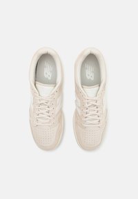 Paire de baskets beige New Balance avec des bouts perforés et des lacets, vue de dessus sur fond blanc.