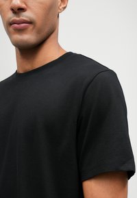 Μαύρο βαμβακερό μπλουζάκι με στρογγυλή λαιμόκοψη και κοντά μανίκια. Το ύφασμα έχει απαλό υφή και εφαρμοστό σχήμα.