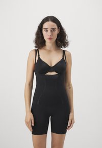 Black shapewear with adjustable straps, cut-out design, and smooth texture, extending to mid-thigh, featuring subtle accent lines.