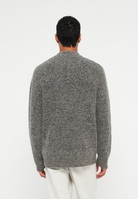 Grå strikket sweater med rund hals og ribbet kant. Materialet virker blødt og tekstureret med et diskret meleret mønster.