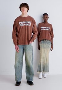 To modeller står side om side. Begge har på seg brune langt ermede skjorter med "PROMISE THE WORLD" i hvitt. Den ene har på seg vide falmede jeans, mens den andre har en lys ombre-skjørt med tarmet kant.