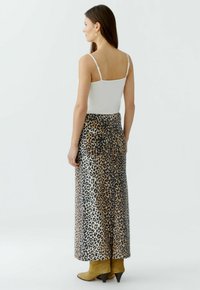 Maxirock im Leopardenmuster mit elastischem Bund, aus glattem Stoff; kombiniert mit einem weißen Tanktop und olivgrünen Ankle Boots.