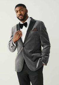 Grauer Samt-Tuxedo-Blazer mit schwarzen Satin-Schalrevers, kombiniert mit einem weißen Hemd, einer schwarzen Fliege und einem gemusterten Einstecktuch.