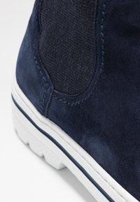 Námořnické semišové kotníkové boty mají texturovanou boční část, bílou podrážku s modrým akcentem a prošívané detaily pro strukturovaný design.