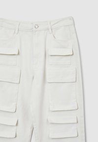 Weiße Cargo-Hosen mit mehreren Klappen-Taschen, Gürtelschlaufen und einem Metallknopfverschluss auf einem hellen Hintergrund.