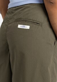 Olive green shorts with a smooth texture, featuring a back pocket and a white tag labeled “Element Skateboard Co.”