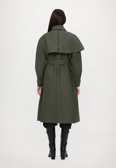 Ελαιοπράσινο παλτό τύπου trench με μεγάλη πίσω πτύχωση, ζώνη στη μέση και κουμπιά. Φτιαγμένο από διαρθρωμένο ύφασμα, διαθέτει μακριά μανίκια και κομψή εφαρμογή.