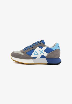 Lage sneaker met grijs suède, blauwe stof, wit geometrisch logo, blauwe veters en een zool van natuurlijke rubber, weergegeven in zijaanzicht op een witte achtergrond.