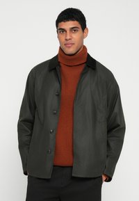 Σκούρο πράσινο μπουφάν με κουμπιά και μαλακό μαύρο γιακά. Φοριέται πάνω από υφασμάτινη, σκουροκόκκινη μπλούζα με γιακά τύπου ζιβάγκο. Απλός, καθημερινός σχεδιασμός.