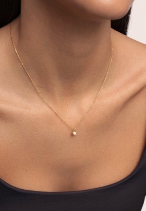Collar de oro con una cadena delgada y un pequeño colgante redondo que presenta un detalle de perla, posicionado elegantemente alrededor del cuello.